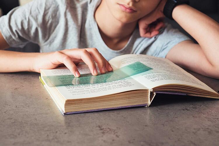Kind mit Legasthenie liest in einem Buch mit Hilfe eines Lesestreifens