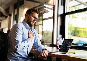 Mann arbeitet am Laptop und greift sich ans Herz