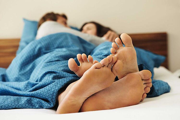 Paar liegt im Bett mit ineinander verschlungenen Füßen.