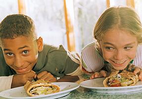 Lachende Kinder vor Tellern mit Wraps.