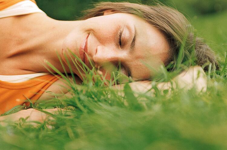 Frau liegt lächelnd und mit geschlossenen Augen im Gras.