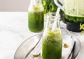 Grüner Smoothie in einer Glasflasche mit einem weißen Strohhalm.