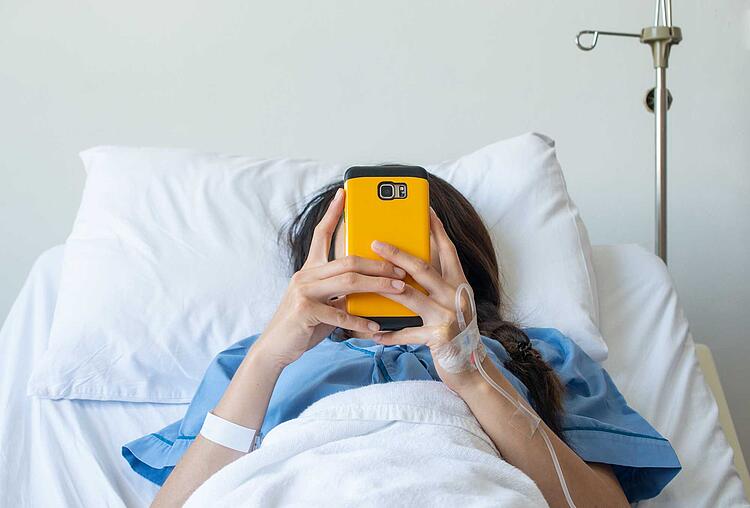 Frau im Krankenhausbett schaut auf ihr Smartphone
