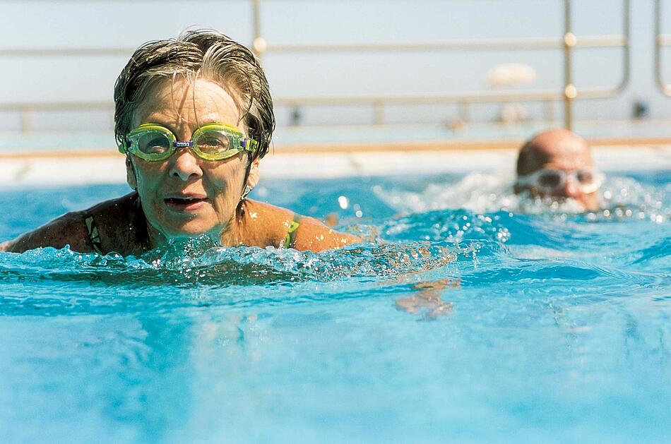 Ältere Frau mit Schwimmbrille schwimmt im Freibad.
