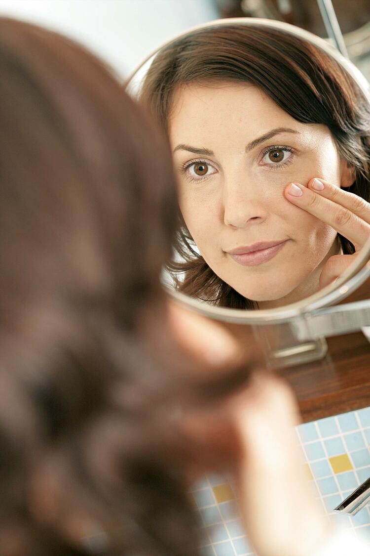 Eine Frau untersucht ihre Gesichtshaut in eienm Kosmetikspiegel.