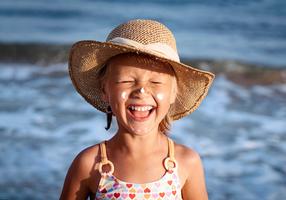 Mädchen mit Sonnenhut und Sonnencreme im Gesicht am Strand