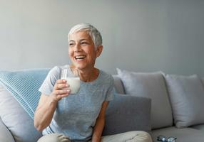 Lachende Frau hält ein Glas MIlch in der Hand