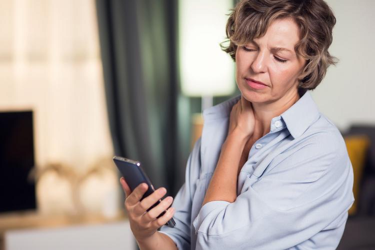 Bildnachweis: © stock.adobe.com / Aleksej Frau mit Smartsphone in der Hand greift sich an den schmerzenden Nacken