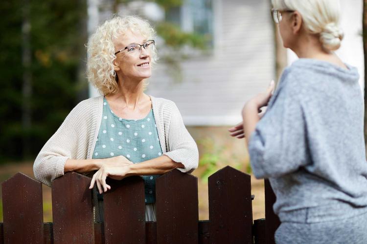 Zwei Frauen unterhalten sich über den Gartenzaun hinweg