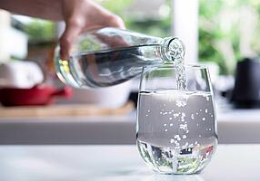 Hand gießt Mineralwasser aus einer Flasche in ein Glas