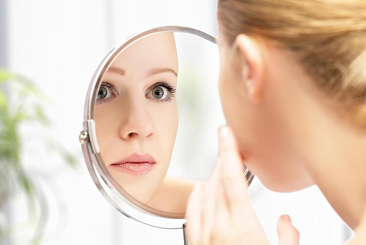 Frau schaut in Kosmetikspiegel