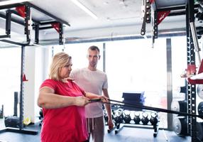 Übergewichtige Frau trainiert im Fitnessstudio unter der Anleitung ihres Trainers.