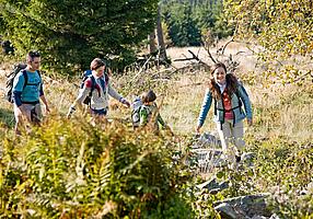 Familie wandert durch Gestrüpp am Waldrand entlang.