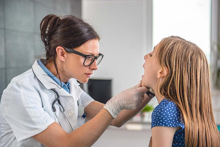 Eine Ärztin untersucht ein Mädchen und schaut ihr in den Hals.