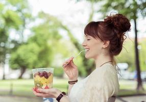 Junge Frau genießt einen Obstsalat unterwegs im Park