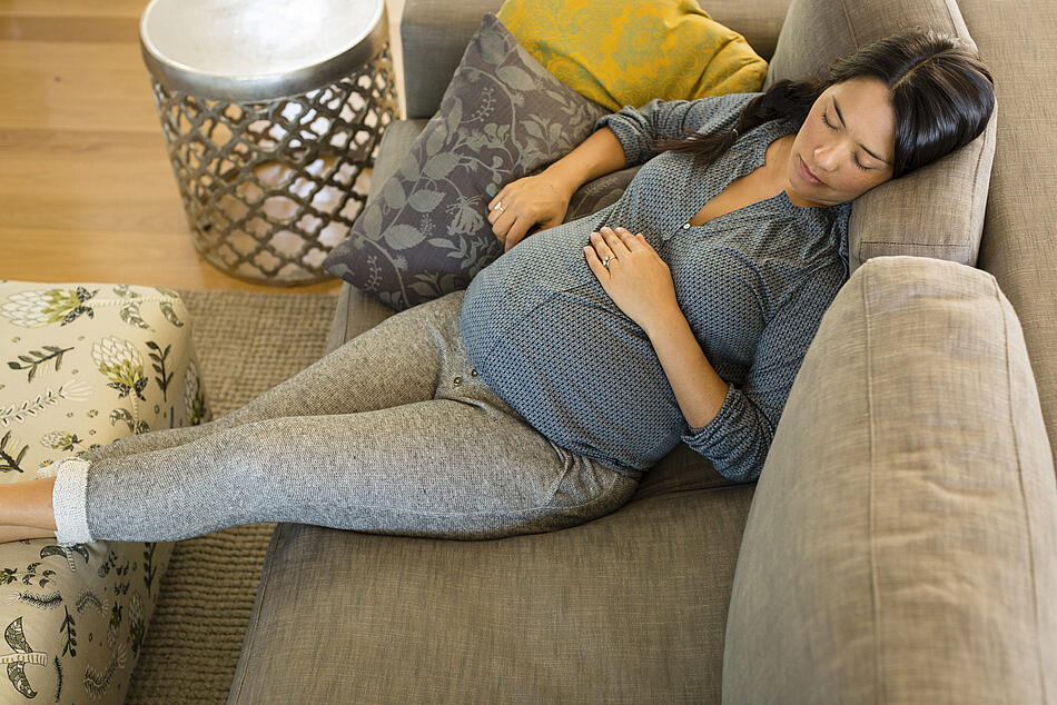 Schwangere sitzt auf dem Sofa , hat die Augen geschlossen und die Füße hochgelegt.