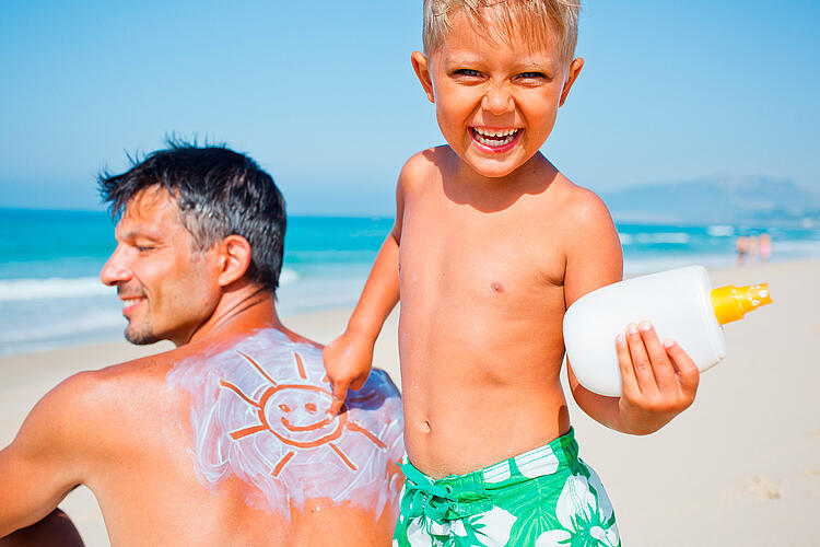 Vater und Sohn am Strand, der Vater hat eine in Sonnenmilch gemalte Sonne auf dem Rücken