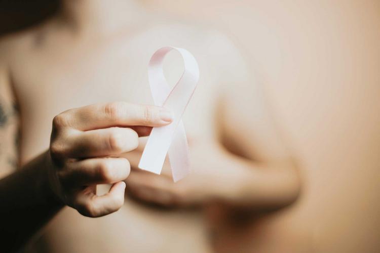 Bildnachweis: © a-c-Fispz0hXTsM-unsplash Frau mit nacktem Oberkörper bedeckt ihre Brust und hat eine Brustkrebs-Schleife in der Hand