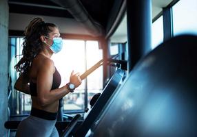 Frau mit Mundschutz auf dem Laufband im Fitnessstudio