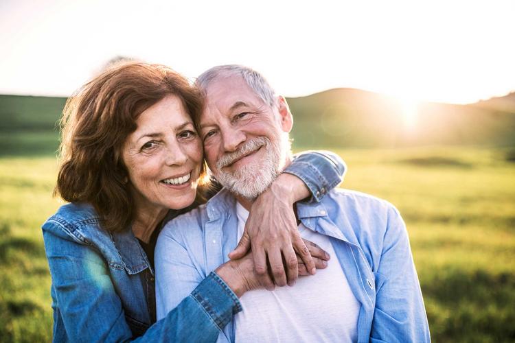 Älteres Paar in der Natur, Frau umarmt den Mann und beide lächeln in die Kamera