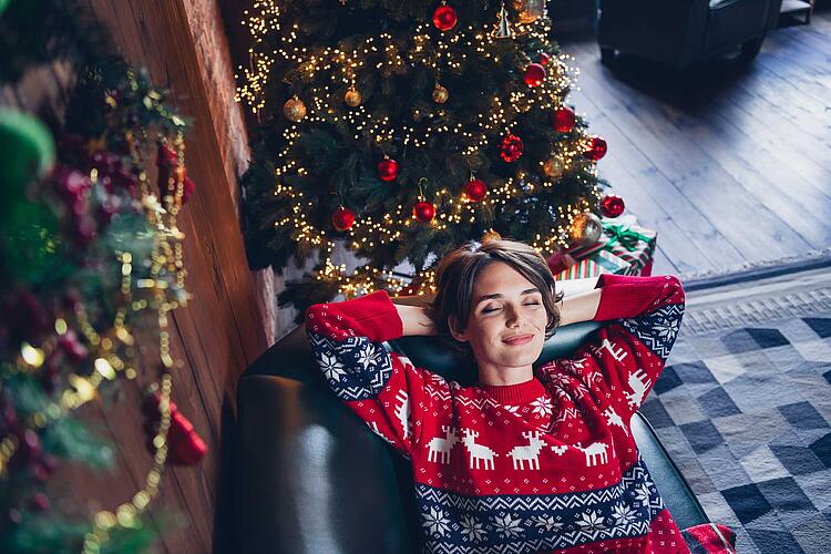 Stress an Weihnachten – Frau chillt auf dem Sofa, daneben steht ein Weihnachtsbaum