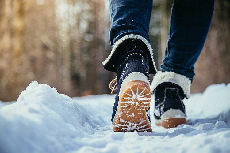 Frauenbeine mit Winterstiefeln laufen im Schnee
