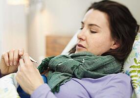 Frau mit Fieberthermometer in der Hand.