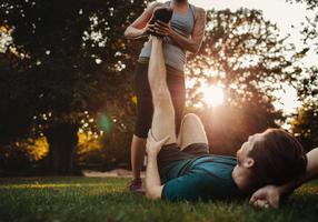 Ein Mann bekommt beim Joggen einen Wadenkrampf, eine Frau dehnt sein Bein