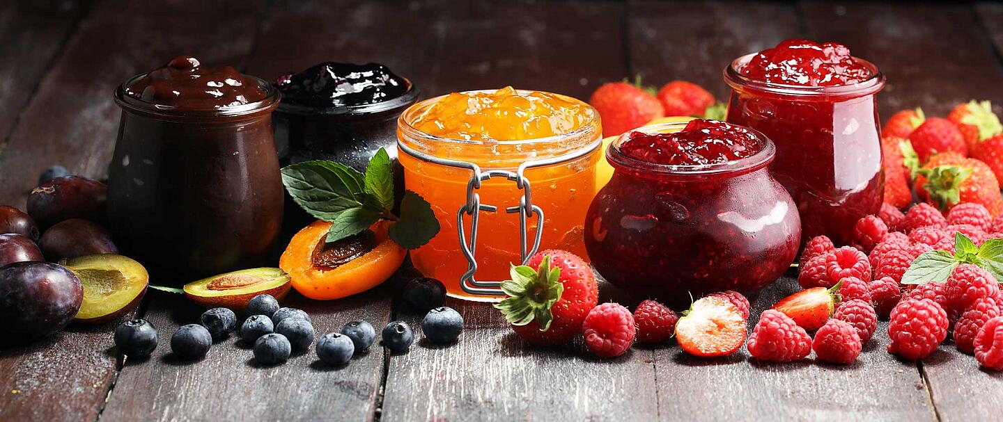 Verschiedene Sorten Marmelade in Gläsern und Früchte auf einem Holztisch