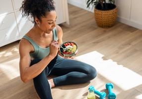 Frau iss einne Früchte Bowl nach dem Training zu Hause auf dem Fußboden in der Küche