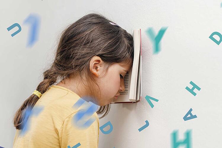 Kinder in der Stressfalle: Mädchen lehnt mit Buch vor der Stirn ihren Kopf an die Wand