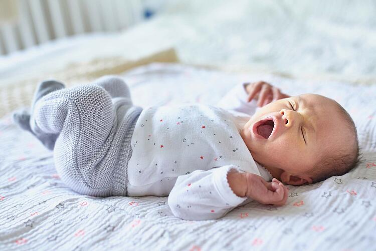 Ein Säugling liegt gähnend auf einer Decke