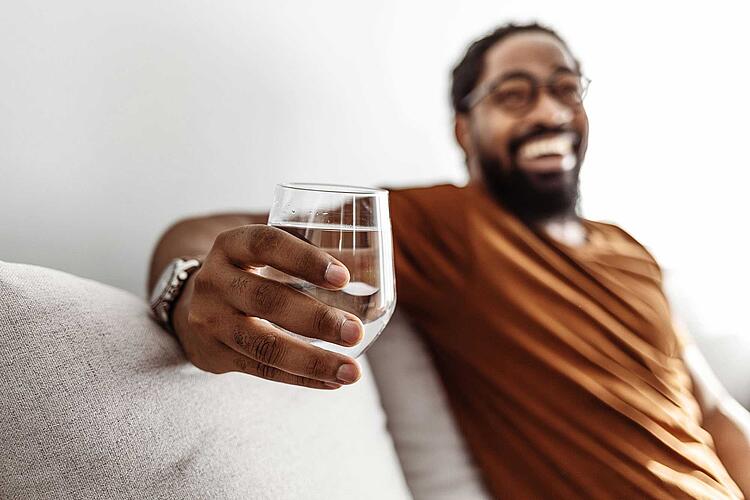 Lachender Mann hält ein Glas Wasser in der Hand.