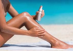 Frau cremt am Strand ihre Beine mit Sonnencreme ein