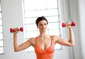 Junge Frau in Sporttop trainiert mit Kurzhanteln in einem Fitnessstudio.