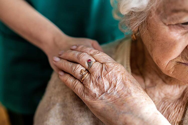 Ältere Frau legt ihre Hand auf die Hand ihrer Pflegerin