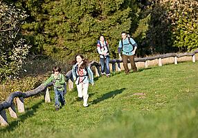 Familie wandert an einem Holzaun entlang über eine Wiese.